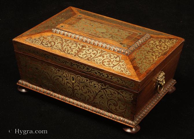 Antique box in the sarcophagus form. The box is veneered in figured rosewood and is inlaid in brass depicting stylized flora. The fluid design of stylised flora is exceptionally fine. This is a spectacular box which encapsulates the best of the Regency era. The box stands on turned rosewood feet and has brass lion head  drop ring handles. The centre panel of the top is framed with gadrooning as is the pediment adding the architectural impact. The box has a lift out tray which has been relined . Circa1825.  Enlarge Picture